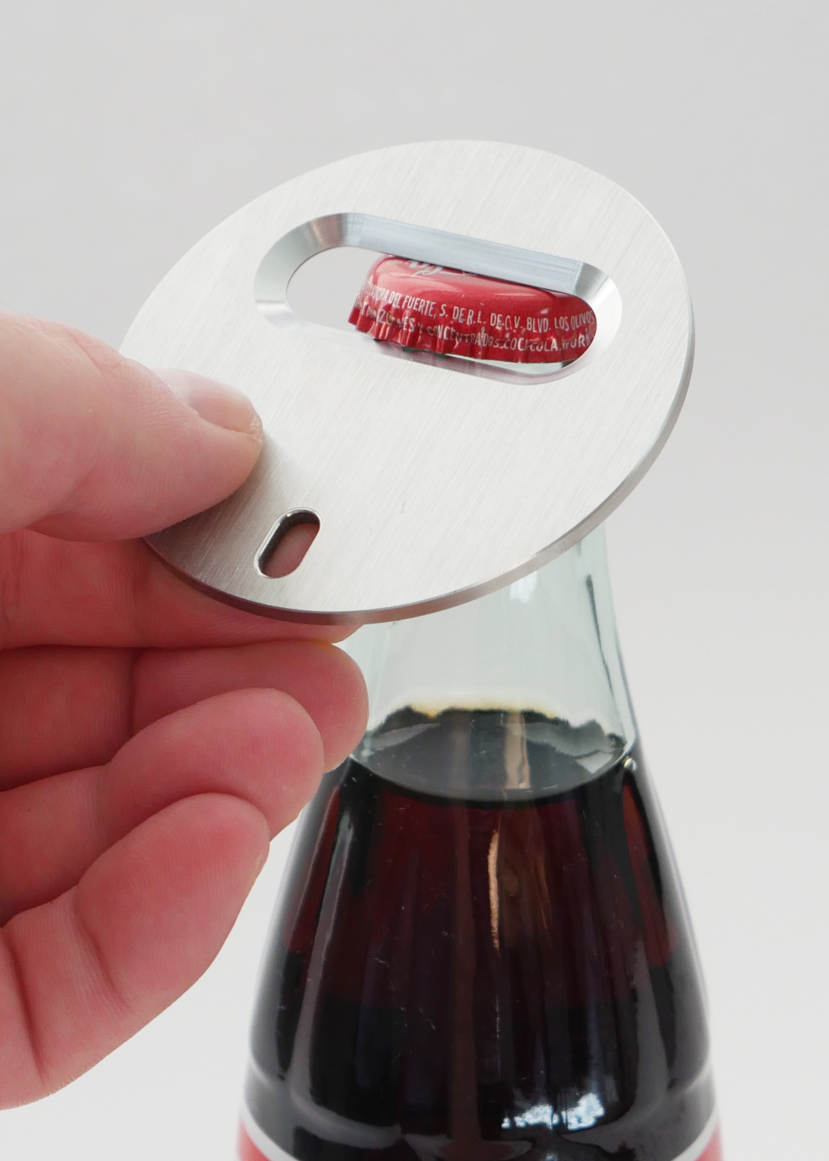 Hand holding metal circle bottle opener opening glass soda bottle